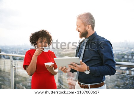 A portrait of two businesspeople with tablet standing against London view panorama.