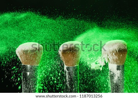 Make up, beauty and mineral powder concept - brush on black background with green powder splashed on it