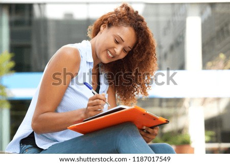 Side portrait of young woman sitting and writing in book with pen