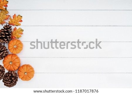 Rustic fall background of autumn leaves, pine cones and mini pumpkins with free copy space for text over a white rustic background. Image shot from overhead.