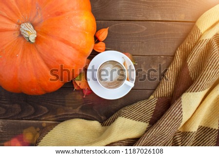 A cup of coffee with cappuccino and autumn leaves and pumpkin on old wooden background. Autumn decor, fall, thanksgiving day mood, autumn still life.