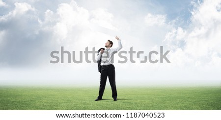 Successful and confident businessman in suit starting launching huge white arrow to the air while standing on green lawn and cloudy skyscape view on background