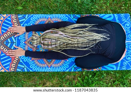 blonde girl with dreadlocks doing yoga in the park on the rug
