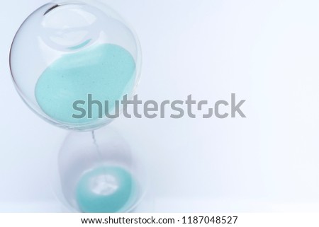 Hourglass on white background. Sand falls inside an azure-colored flask.