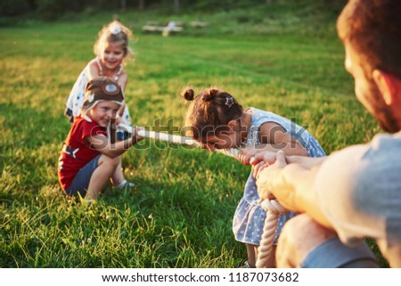 Children play with dad in the park. They pull the rope and have fun laying on a sunny day.