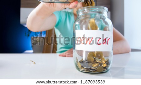 Closeup image of young woman filling moneybox for purchasing new car with golden coins