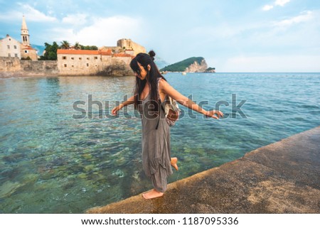woman walking on pier side with Stari Grad (Old Town) on background in Budva, Montenegro 
