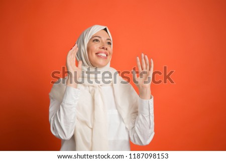 Happy surprised arab woman in hijab. Portrait of smiling girl, posing at red studio background. Young emotional woman. The human emotions, facial expression concept. Front view.