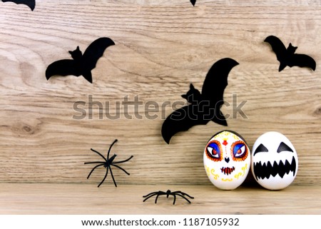 Halloween decoration: black silhouette of bats and spiders with scary spooky skeleton santa muerte eggs with face on wooden background. Halloween holiday concept