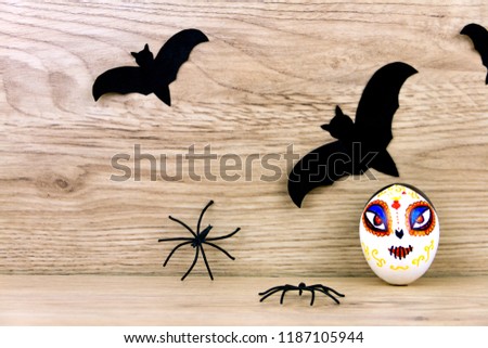 Halloween decoration: black silhouette of bats and spiders with scary spooky skeleton santa muerte eggs with face on wooden background. Halloween holiday concept