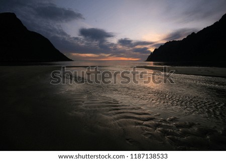 Little stream on a beach against ocean and mountains at sunset