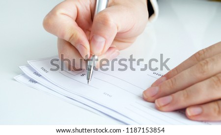 Closeup photo of female hand signing banking cheque