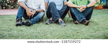 Three men wearing jeans sitting together on the grass. Close up shot of group of adults with smart casual dress relaxing on the green lawn.