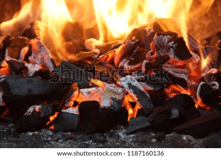 Embers with flames in the barbecue. Front view,in outside and without character. The embershave a beautiful yellow, orange bright color.