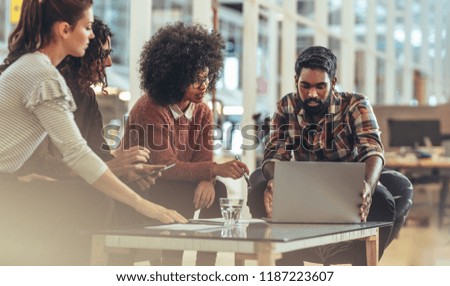 Business partners in a meeting discussing ideas sitting in office. Businessman working on laptop sitting with female coworkers in office.