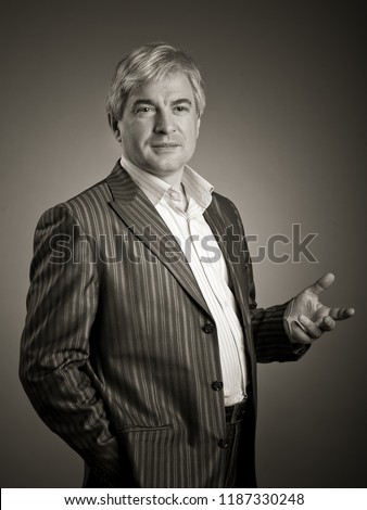 Animposing respectable grey-haired man. A handsome imposing respectable grey-haired man wearing a jackethas raised his hand with a gesture of greeting.