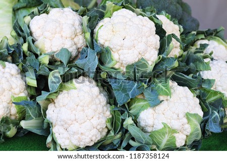 fresh cauliflower with white heads and green leaves stacked up at weekly market Royalty-Free Stock Photo #1187358124