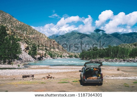 Car with open large trunk near mountain river with turquoise water. Tourists on vacation in mountains. Tourist things in car. Journey and active rest in highlands. Travel background.