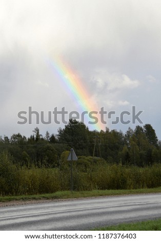 Bright rainbow over forest at countryside on a rainy autumn day.
