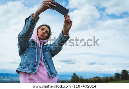 tourist girl on background blue sky clouds taking photo selfie on mobile smart phone, person looking on camera gadget technology, blogger using content online wifi internet lifestyle concept