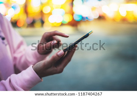 Person pointing finger on screen smartphone on defocus background bokeh light in evening street, hipster girl using in hands mobile phone gadget in night atmospheric city, online wifi internet concept
