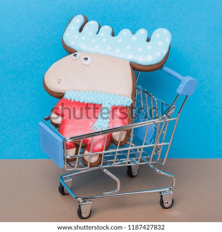 concept of Christmas shopping, honey gingerbread in the shape of an elk sits in a supermarket cart on a blue background, a minimal