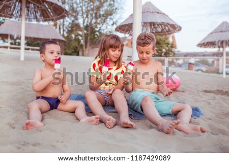 Happy positive children sitting on the sandy beach and eating ice cream. People, children, friends and friendship concept