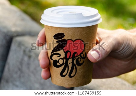A hand with a street cup of coffee with the inscription "I love coffee."