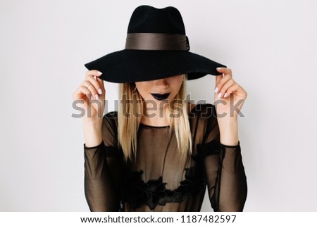 Close-up inside portrait of dreamy elegant woman in black hat covering face, model girl portrait with trendy gothic black make up. Halloween Vampire Woman with black matte lips