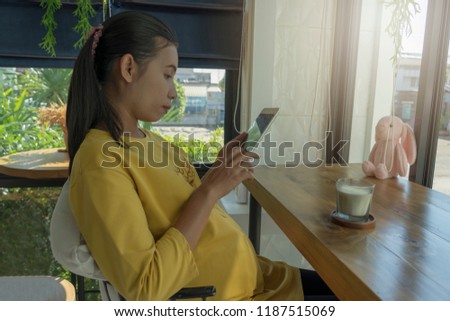 A portrait of a beautiful pregnant woman using tablet
and a glass of milk in the coffee shop.