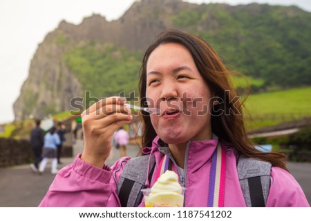 An Asia Chinese lady eat an ice cream, with background of volcanic cone in Jeju-island, Korea