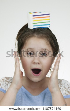 The vertical picture of a surprised girl with a squishy layered cake on the top of her head and hands near the face over white background