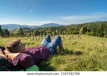 The travel photographer is resting on a clearing in the forest and looking at the mountains