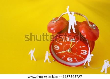 miniature paper people with  a large clock, an alarm clock on a yellow background. The concept of time and man