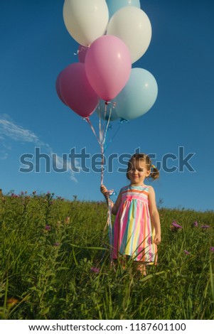 Pretty girl  holding blue, pink and white balloons in the field with the blue sky