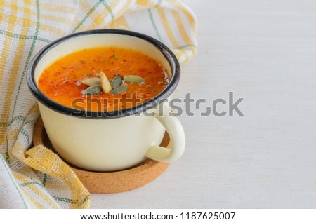 Homemade pumpkin soup with  spice and pumpkin seeds in metallic mug  on wooden table. Traditional autumn food for healthy lifestyle.Copy space
