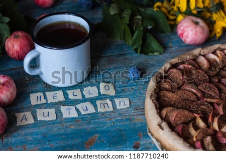 Apple pie on wooden blue rustic background. Hello autumn picture. Apples, tea in a metal countre cup, yellow flowers and plums.
