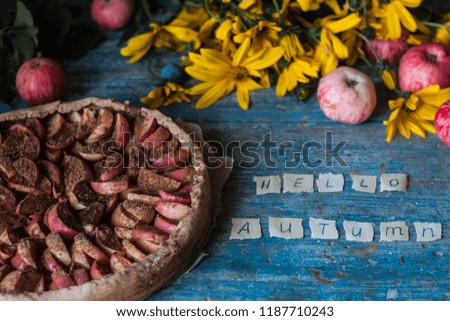 Apple pie on wooden blue rustic background. Hello autumn sign picture. Apples, yellow flowers and plums.