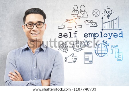 Smiling Asian man in glasses and shirt standing with crossed arms near a concrete wall with self employed text and icons on it. Toned image