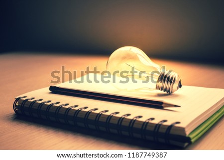 Blank notebook and pencil with light bulb on wooden table.creative ideas of writer, thinking for work on desk