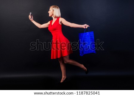 attractive blond woman in red dress holds a leather blue bag in high heels full-length studio shot in black background. black Friday shopping sale concept