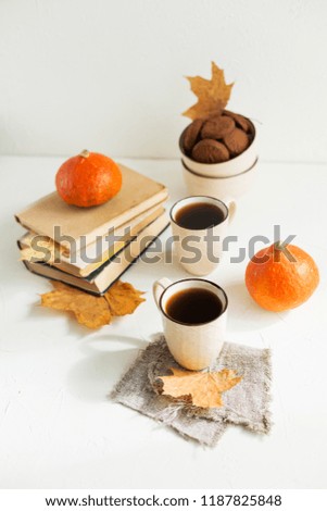 Hot tea in beige cups, dry maple leaves, old books and oat chocolate cookies on white table. Autumn composition.