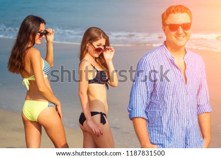 two beautiful women look with enamored eyes at a single man walking along the beach