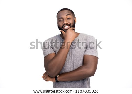 Clever confident dark skinned male model, gentle smile, clever look, being sure in his success, wears round spectacles and casual t-shirt, stands indoor against white background. Friendly looking guy