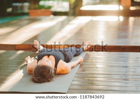 Unrecognizable young woman working outdoors, doing yoga exercise on grey mat, lying in Shavasana - Dead Body Posture, resting after practice, meditating, class. Tropical island Bali. Royalty-Free Stock Photo #1187843692
