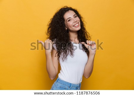 Photo of beautiful excited young cute woman posing isolated over yellow background pointing.