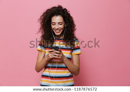 Image of an excited happy cute young woman posing isolated over pink background using mobile phone listening music.