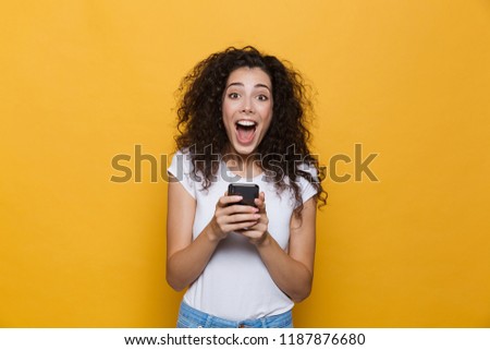 Image of an excited happy cute young woman posing isolated over yellow background using mobile phone.