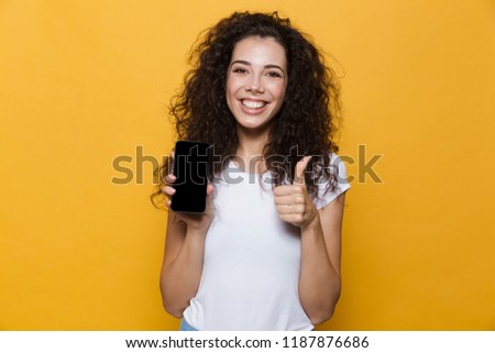 Image of an excited happy cute young woman posing isolated over yellow background showing display of mobile phone make thumbs up.