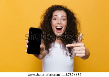 Image of an excited happy cute young woman posing isolated over yellow background showing display of mobile phone.
